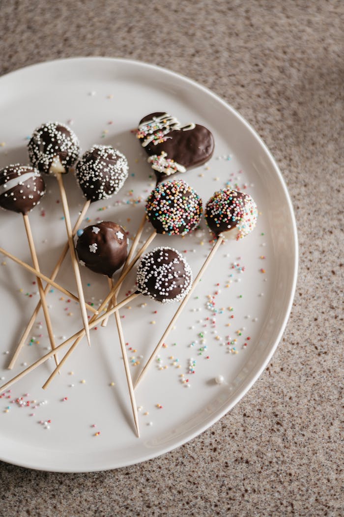 Delicious chocolate cake pops with colorful sprinkles on a white plate, perfect for dessert lovers.