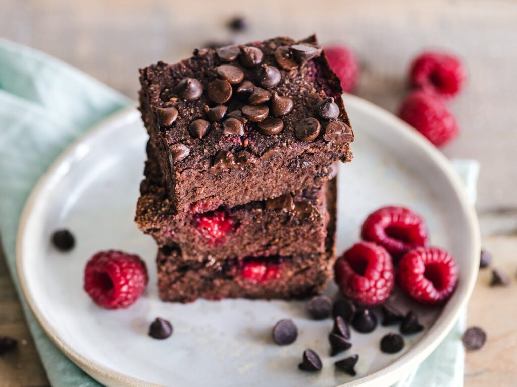 pexels-photo-3026804 Close-up of deliciously indulgent chocolate raspberry brownies stacked on a ceramic plate with fresh raspberries.